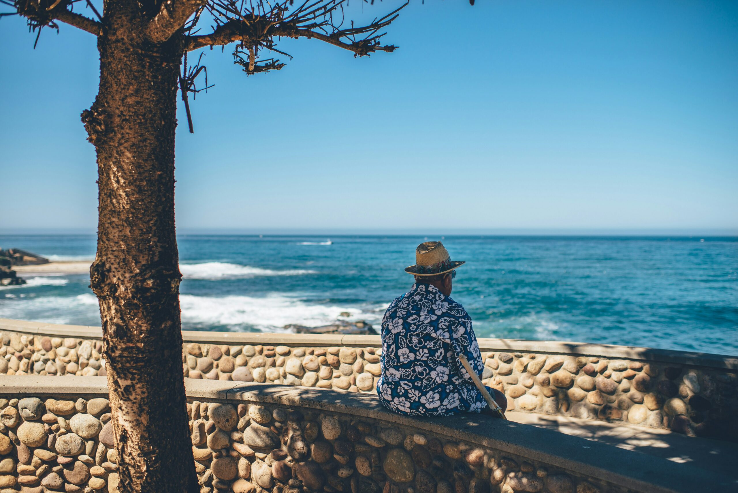 A man in an Aloha shirt sits beside the ocean
