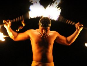 A fire-knife dancer holds two flaming blades behind his back while performing at a Hawaiian luau.