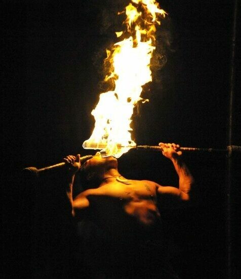 Fire knife danceer performs, placing two flaming blades to his mouth
