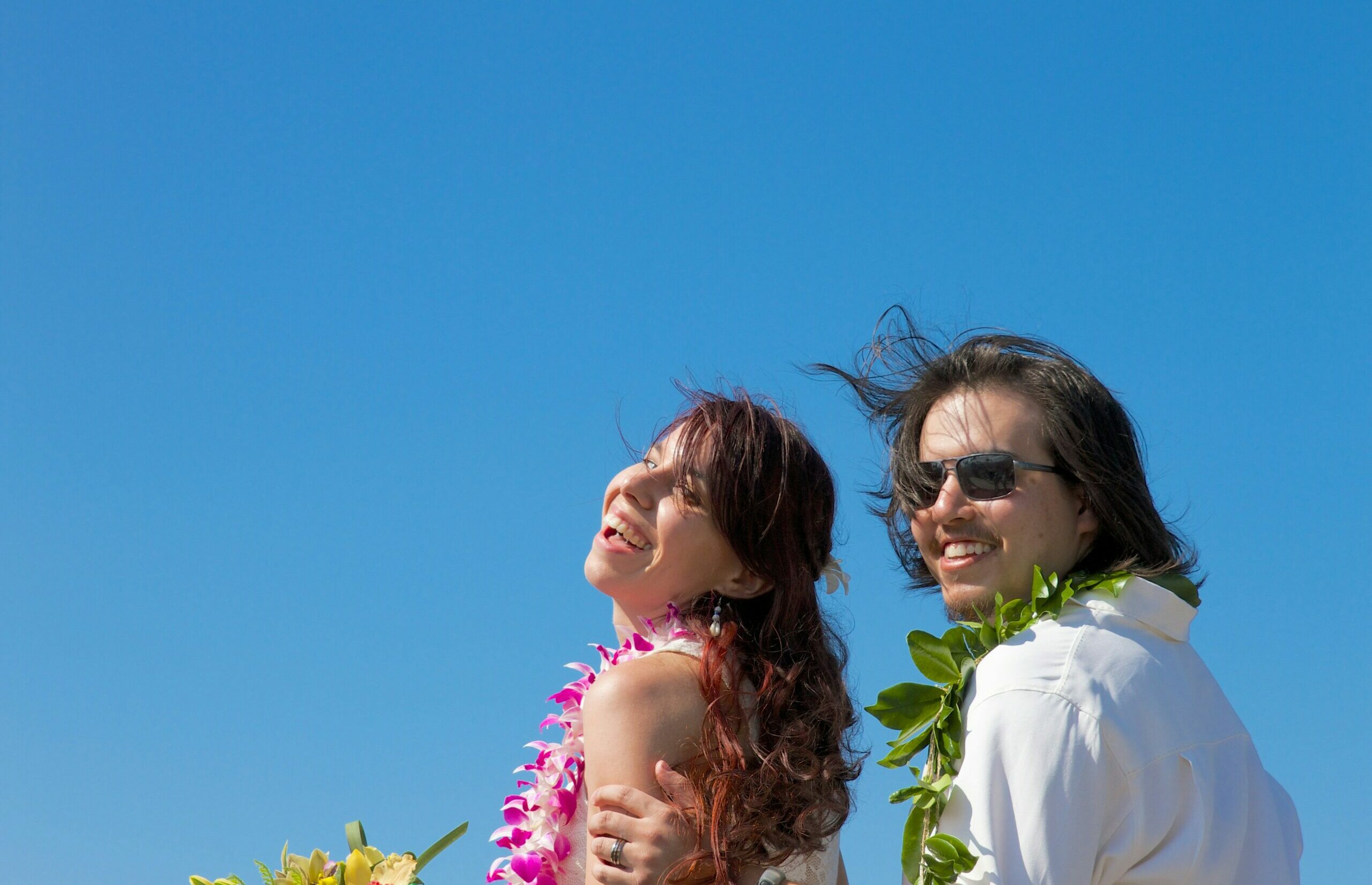 Smiling couple wearing leis with blue sky in background