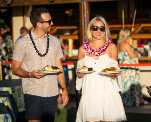 Couple holding three plates of food at a luau.