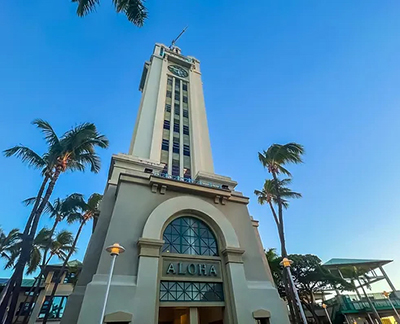 Aloha Tower in Honolulu Hawaii under a blue sky surrounded by palm trees.
