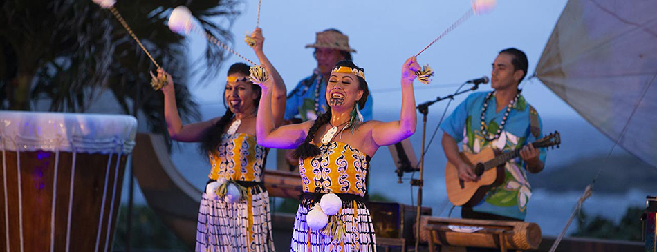 Luau cast members swing poi balls in front of a Hawaiian band. 