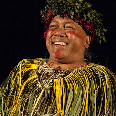 Chief Sielu smiles while performing at luau in grass cape and head dress. 