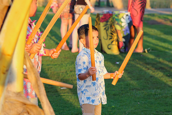 A child learns to play a traditional instrument on the lawn at a luau in Waikiki.