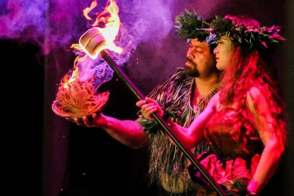 Performers in Hawaiian dress pass fire from torch to coconut to begin the luau ceremony. 