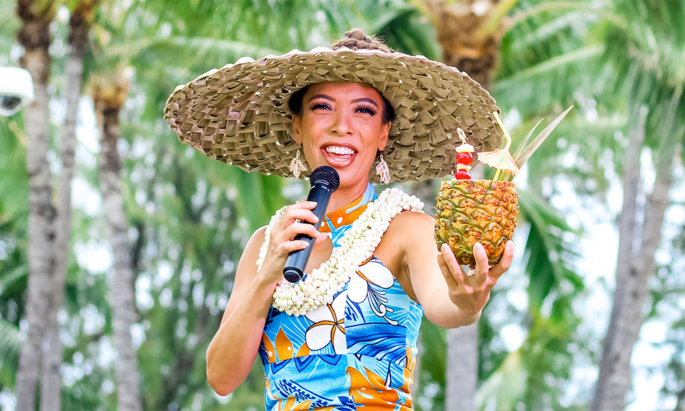 The Luau's Hostess holds a cocktail filled pineapple while performing on stage. 