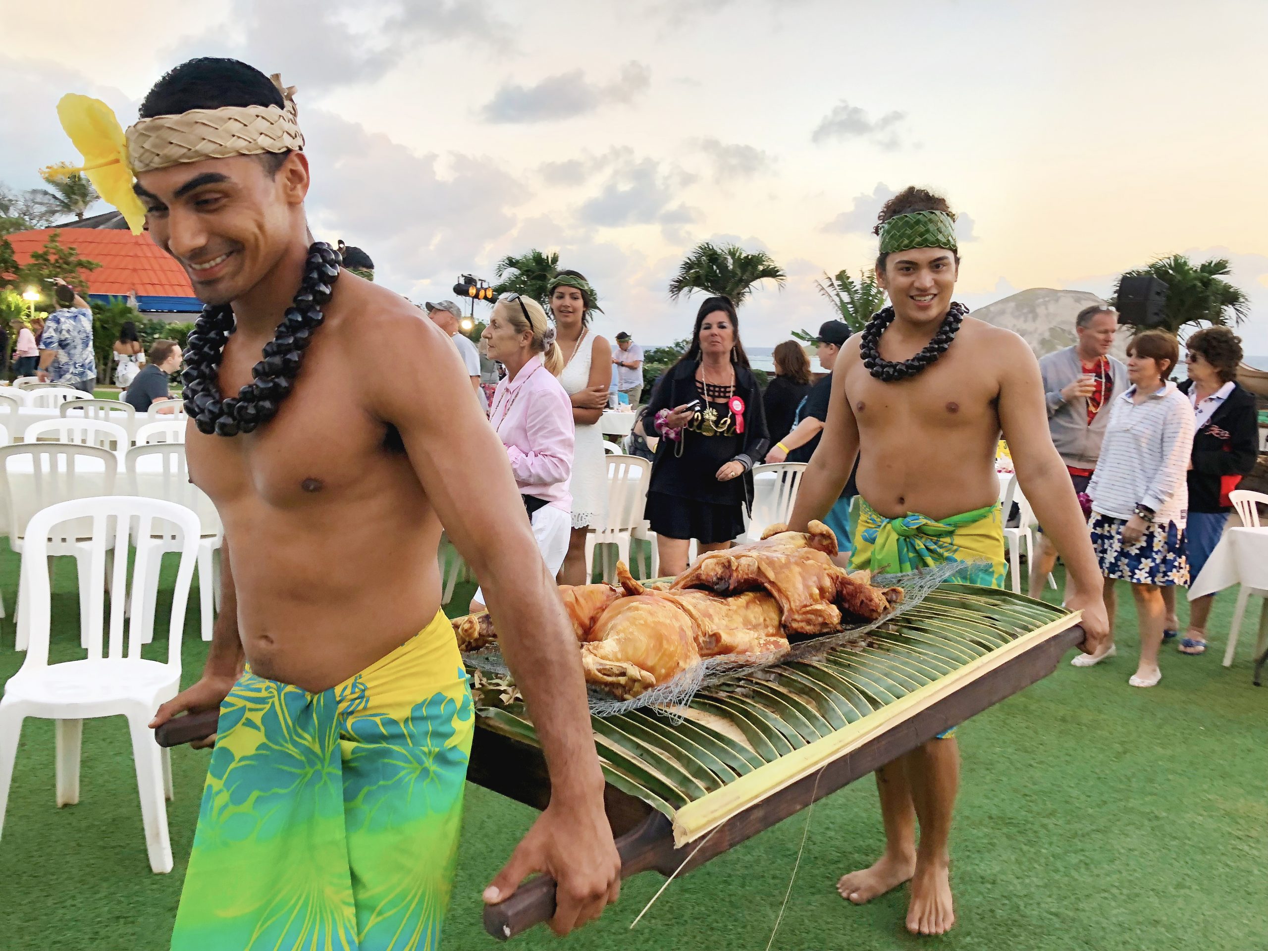 Two men carry a roasted pig at Aloha Kai Luau, Oahu.