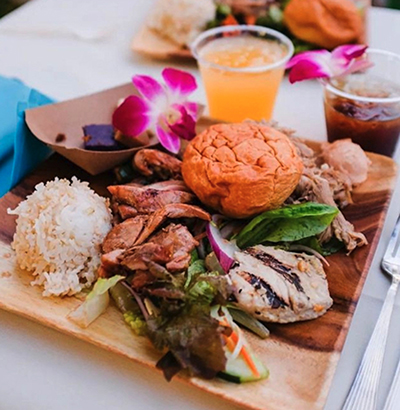A plate of food from the luau buffet with pork, fish, chicken, rice and beverages.