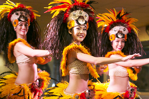 Luau dancers pose is costumes with bright yellow feathers and large headdresses. 