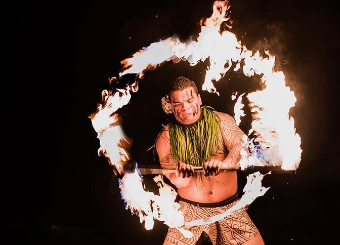 A fire-knife dancer swirls a flaming blade in a circle. 