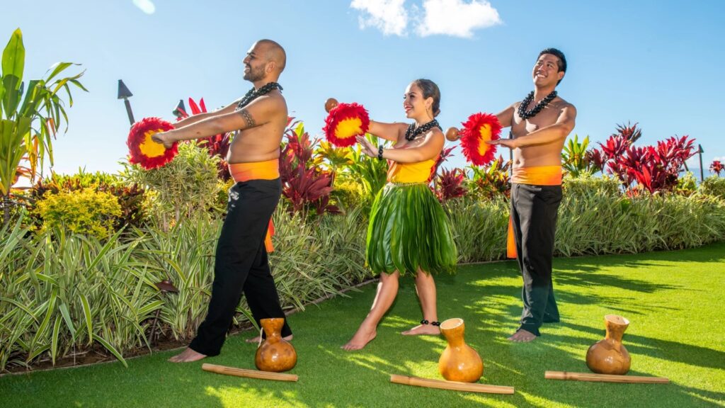 Cast members of the Myths of Maui Luau pose with feathered gourds on the lawn.