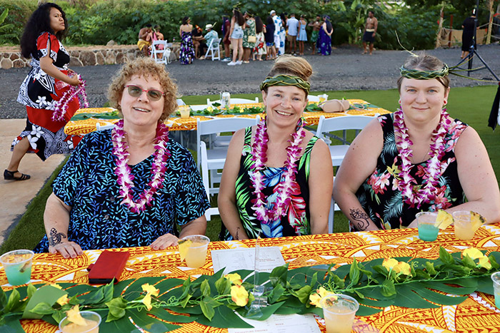 Guests are seated at a luau table wearing flower leis and grass headbands. 