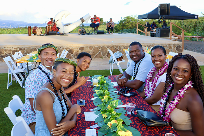 A family is seated in front of the stage while a Hawaiian band plays.
