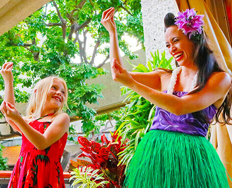 A hula dancer teaches a young luau guest the hula.