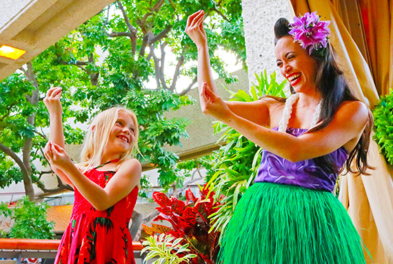 A young girl copies the pose of luau cast member with a purple flower in her hair. 