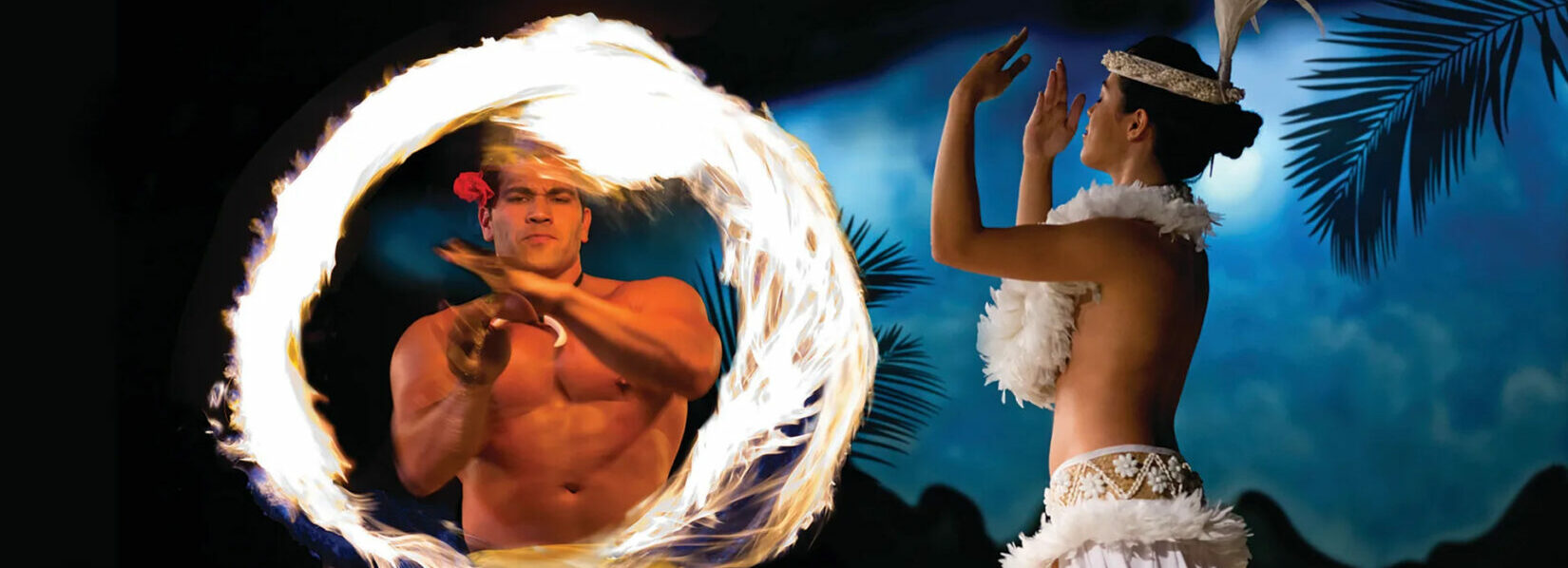 A man spins a flaming torch with a woman dancing the hula at the Hilton Hawaiian Luau.