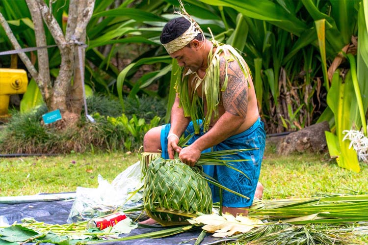 A man weaves a basket from grass as a demonstration for luau guests. 