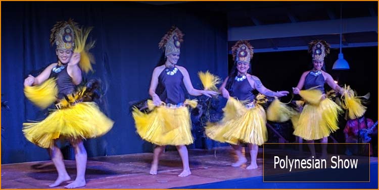 Luau cast members dance on stage in yellow skirts and headdresses. 